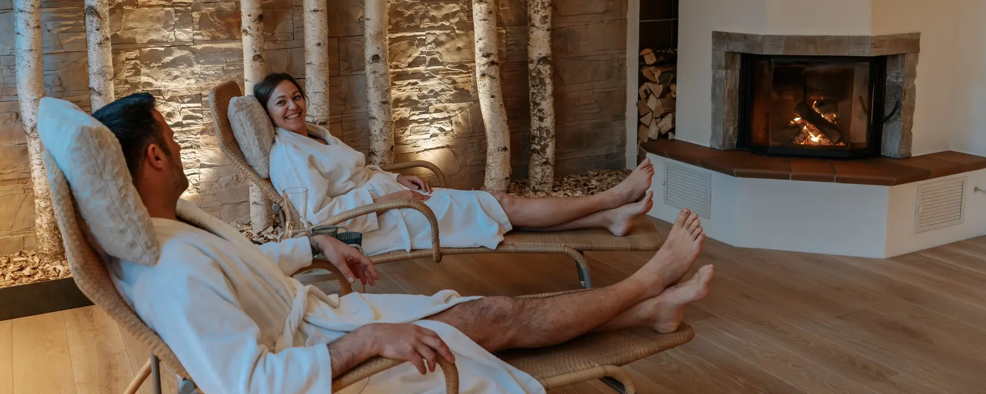 ein Paar liegt im Bademantel auf Liegen vor dem Kamin 