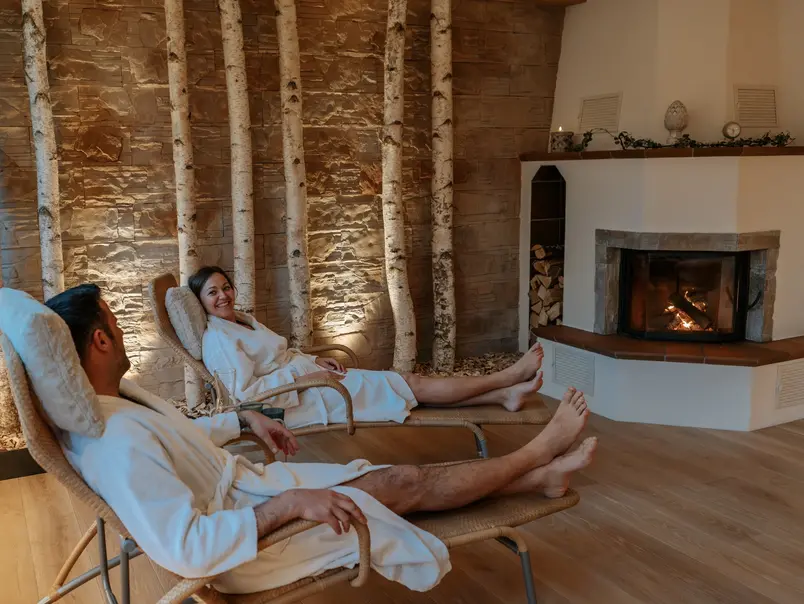 ein Paar liegt im Bademantel auf Liegen vor dem Kamin 