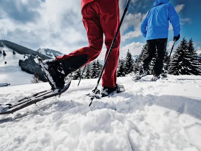 Zwei Personen beim Schneeschuhwandern durch die verschneite Allgäuer Berglandschaft – Winterurlaub auf dem Bauernhof mit Natur und Bewegung genießen.