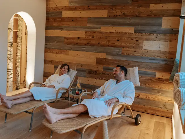 Wellness‑Ruheraum mit Holzverkleidung, sanftem Licht und mehreren Personen, die entspannt auf breiten Holzliegen liegen.