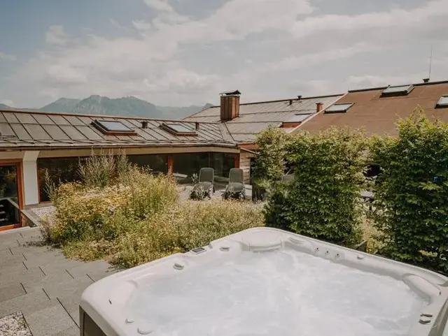 Whirlpool auf einer sonnigen Terrasse im Allgäu mit Blick auf einen idyllischen Bauernhof und alpine Naturkulisse.