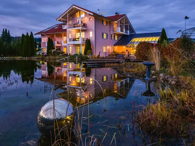 Beleuchteter Wellnesshof im Allgäu bei Dämmerung mit Naturteich und Spiegelung des Hauses in ruhiger, naturnaher Urlaubslage.