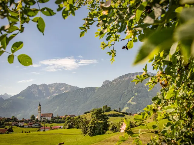 Grüne Wiesen, Dorfkirche und Allgäuer Berge bei Pfronten – ländliche Idylle für einen erholsamen Bauernhofurlaub.