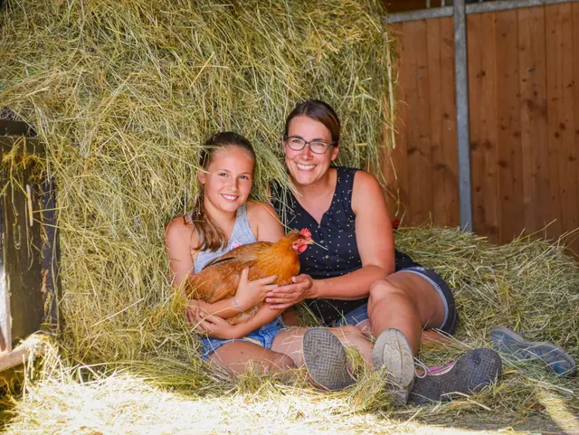 Mutter und Kind sitzen im Heu - auf dem Schoß ein Huhn 
